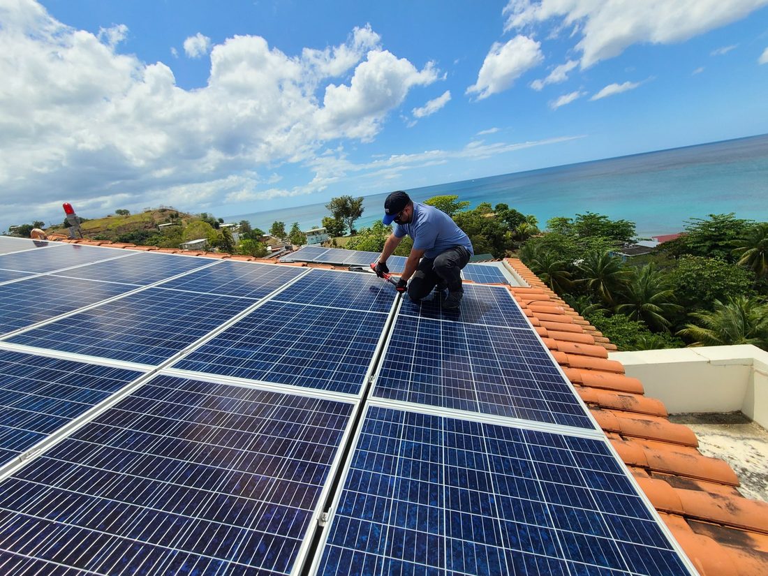 Técnico de Solar Walk dando servicio a paneles solares en un techo de tejas frente al mar